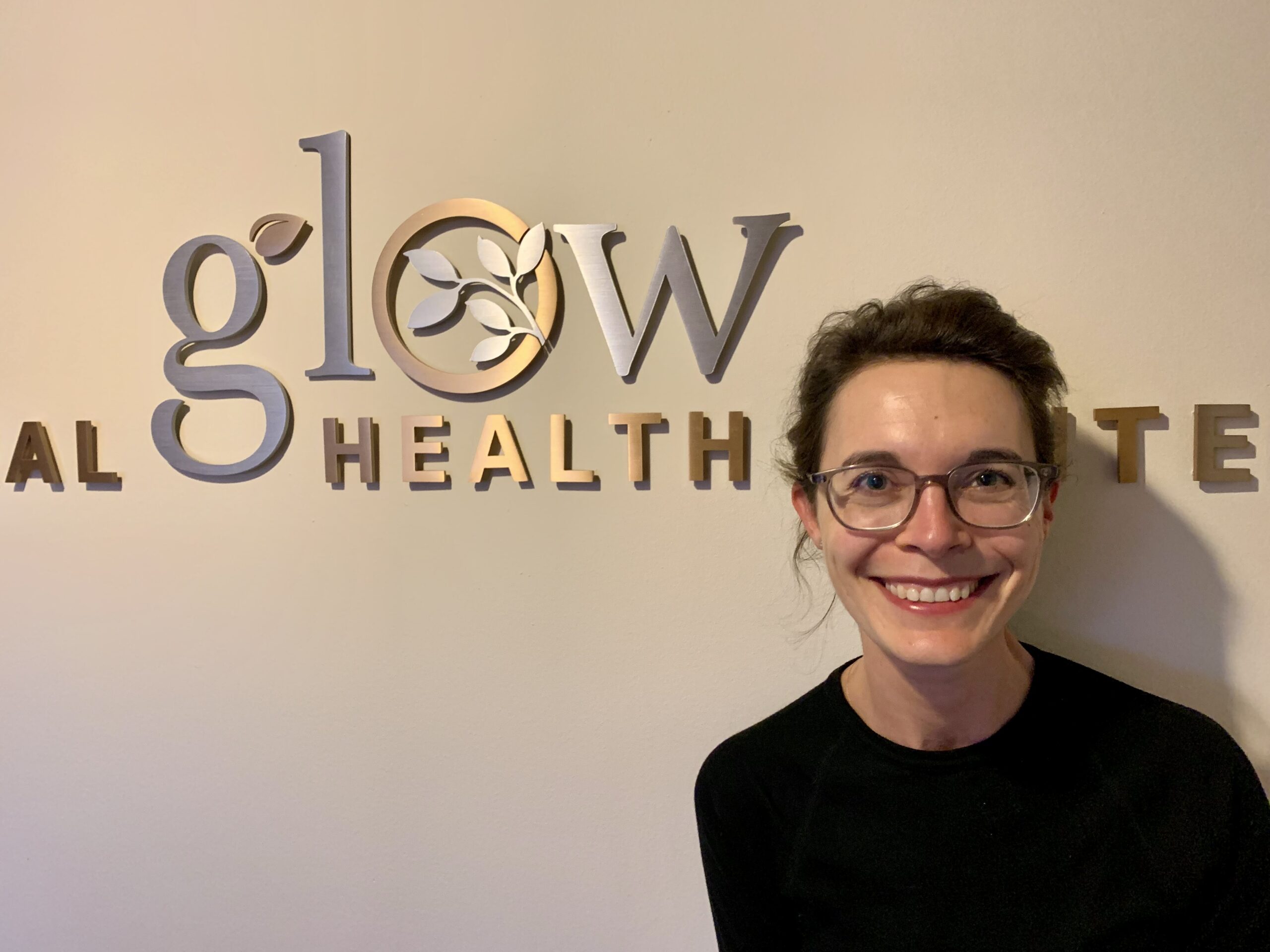 Headshot of acupuncturist Becca Bull in front of Glow sign, Seattle WA